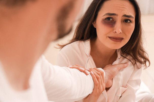 bruised young woman with her husband in bedroom, closeup. Domestic violence concept - Photo, Image