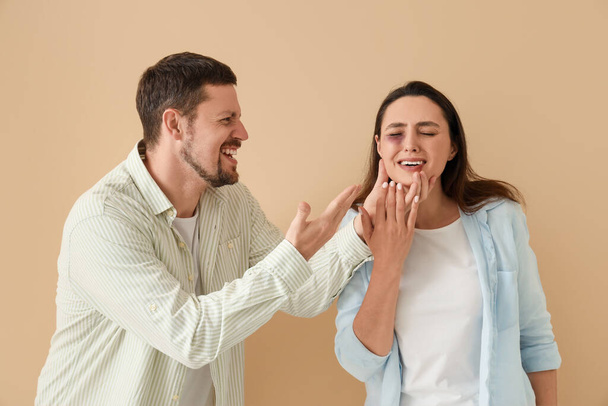 Marido enojado con su esposa magullada sobre fondo beige. Concepto de violencia doméstica - Foto, imagen