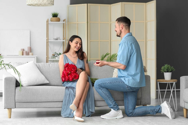 Young man proposing to his girlfriend with flowers at home - Valokuva, kuva