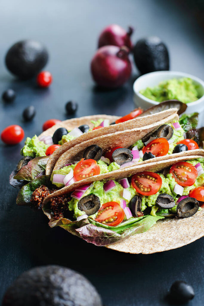 A healthy lunch or dinner of a vegan / vegetarian soft shell taco wrap made with red quinoa with taco season, romaine lettuce, sliced tomatoes, guacamole, black olives and red onions. Selective focus. - Photo, image