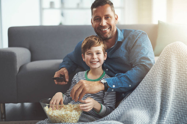 Мальчики смотрят фильмы. Портрет беззаботного мальчика и его отца, смотрящих вместе фильм, сидящих на полу и поедающих попкорн дома в течение дня - Фото, изображение