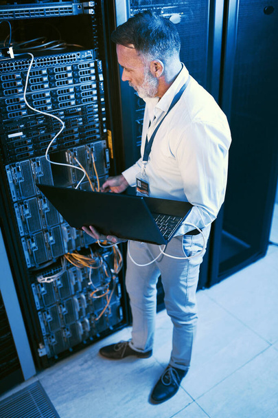 Everything remains safe and secure under his watch. High angle shot of a mature man using a laptop while working in a server room - Valokuva, kuva