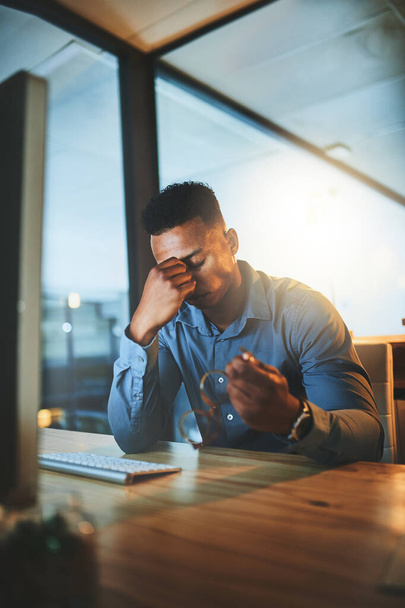Stress veroorzaakt hoofdpijn. een knappe jonge zakenman kijkt gestresst tijdens het werken 's avonds laat in een modern kantoor - Foto, afbeelding