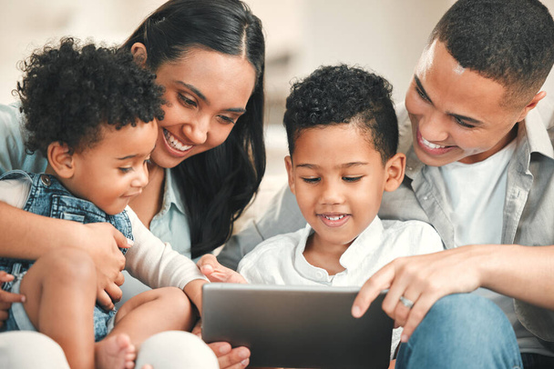Young happy family, kids and tablet on couch for game, movie or learning together in home, love and bonding. Parents, education and children on living room sofa with smile, care or app on touchscreen. - Foto, imagen