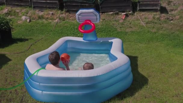 Güneşli bir yaz gününde şişme açık havada yüzme havuzunda arka bahçede su topu oynayan iki çocuk. İsveç. - Video, Çekim