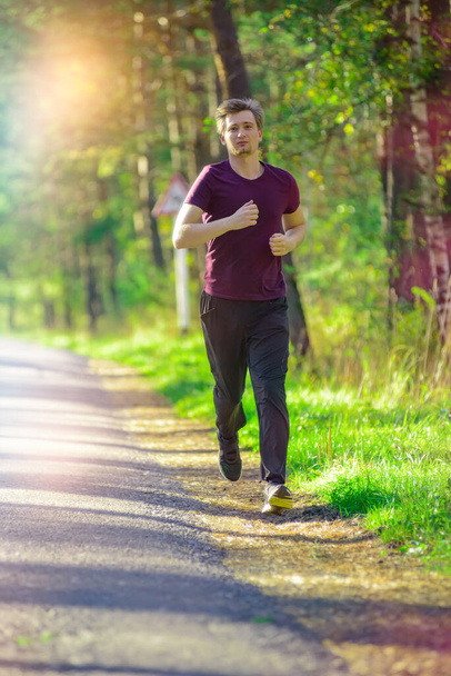 Running man jogging in city park at beautiful summer day. Sport fitness model caucasian ethnicity training outdoor. - Foto, Bild