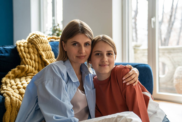 Family portrait smiling mother and daughter looking camera. Parent and daughter spend time together home. Close relationship between child and parent. Mom hug girl, shows love, gratitude, affection - Photo, Image