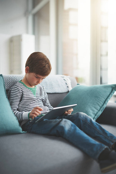 Küszködöm az utolsó számításokkal. egy fókuszált kisfiú nézegeti a digitális táblagépet, miközben otthon ül a kanapén napközben - Fotó, kép