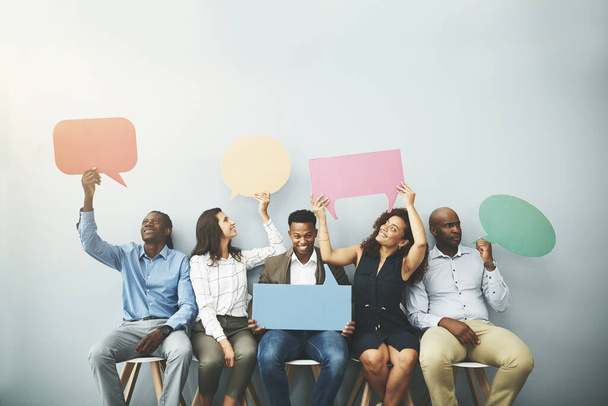 Spreek en zeg wat je te zeggen hebt. Studio shot van een groep zakenmensen met kleurrijke spraakbellen in lijn tegen een grijze achtergrond - Foto, afbeelding