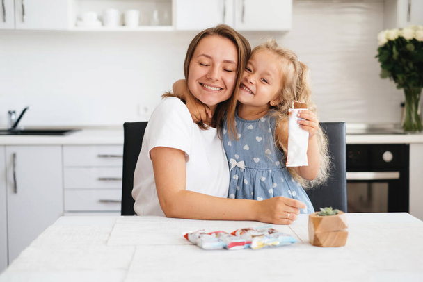 Child is having sweet snack on the kitchen. Happy toddler kid having tasty candy with mother at home. Caucasian blonde family - Valokuva, kuva