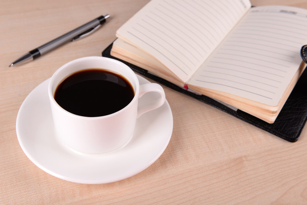 Cup of coffee on saucer with diary and pen on wooden table background - Φωτογραφία, εικόνα