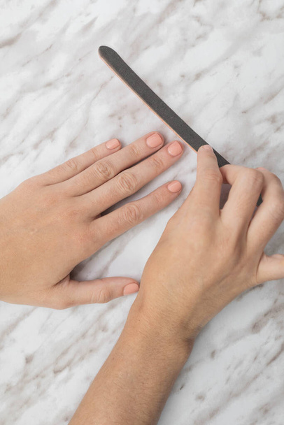 Manicure self care, using nail file, textured studio in the background, glamorous lifestyle and wellness, relaxing activity - Фото, изображение