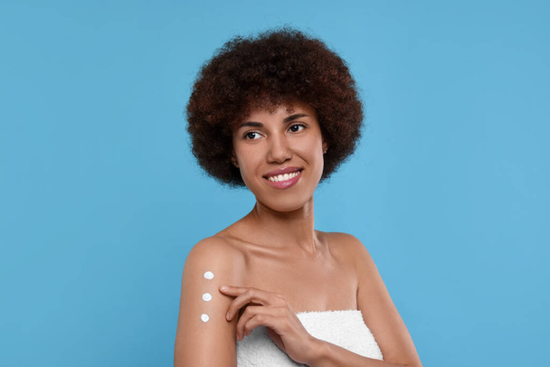 Beautiful young woman applying body cream onto arm on light blue background - Foto, afbeelding