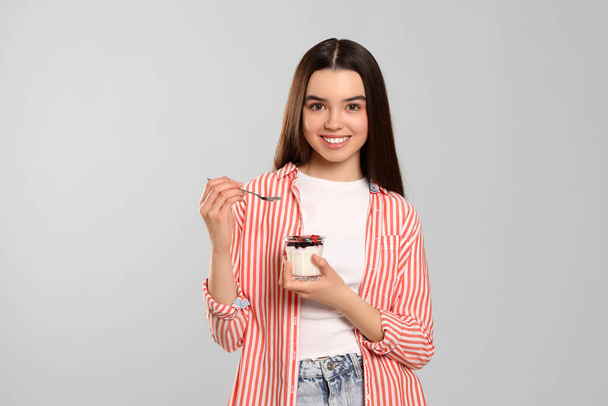 Happy teenage girl with delicious yogurt and spoon on light grey background - Foto, Imagen