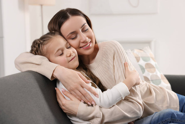 Happy mother hugging her cute daughter on sofa at home - Φωτογραφία, εικόνα