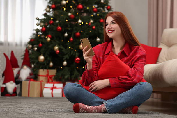 Beautiful young woman using smartphone near Christmas tree at home, space for text - Foto, imagen