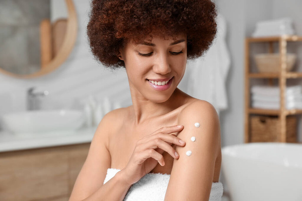 Beautiful young woman applying body cream onto arm in bathroom - Фото, зображення