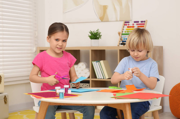 Girl with scissors and boy using glue stick at desk in room. Home workplace - Photo, Image