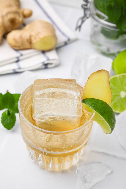 Glass of tasty ginger ale with ice cube and ingredients on white table, closeup - Photo, Image