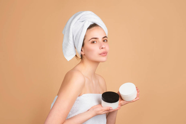 Face mask, spa beauty treatment, skincare. Woman with cream bottle. Beautiful young woman with clean perfect skin. Gestures for advertisement. Beige background. - Foto, Imagen