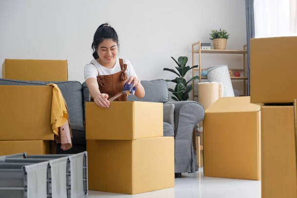 Happy single young woman packing stuff among plenty of cardboard boxes cardboard boxes while moving to new house. Living alone. Modern female people in moving home apartment leisure indoor activity - Foto, afbeelding