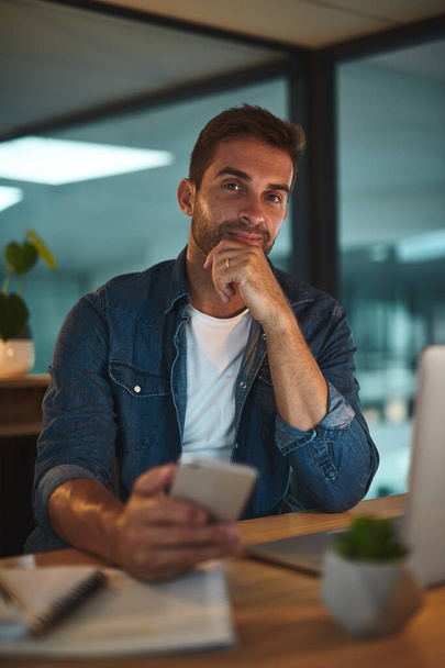 Tomar grandes decisões. Retrato de um belo jovem empresário usando seu celular enquanto sentado em sua mesa em um escritório moderno - Foto, Imagem