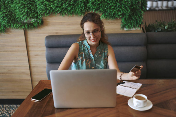 Кредит дает вашему бизнесу реальный импульс при правильном использовании. молодая женщина с помощью ноутбука и кредитной карты во время работы в кафе - Фото, изображение