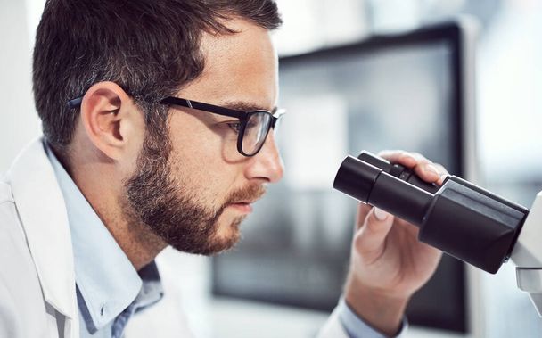 Nunca veo lo mismo cada vez. un joven científico enfocado mirando a través de un microscopio mientras está sentado dentro de un laboratorio - Foto, imagen
