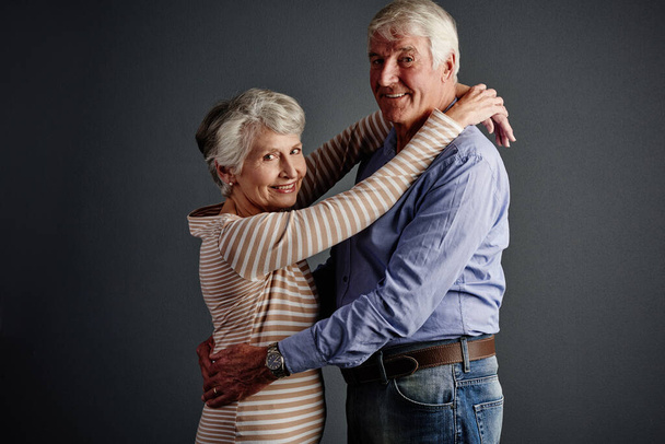 Ill stay in his arms forever. Studio portrait of an affectionate senior couple posing against a grey background - Fotó, kép