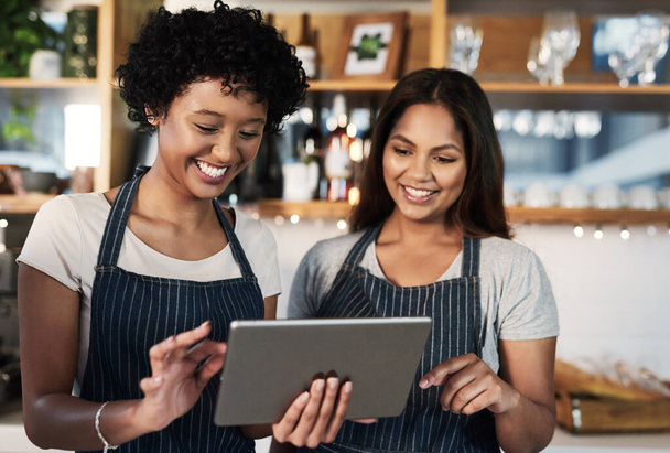Happy woman, tablet and waitress in teamwork at cafe for inventory, checking stock or orders at restaurant. Barista women or small business team working on technology at coffee shop in online service. - Photo, image