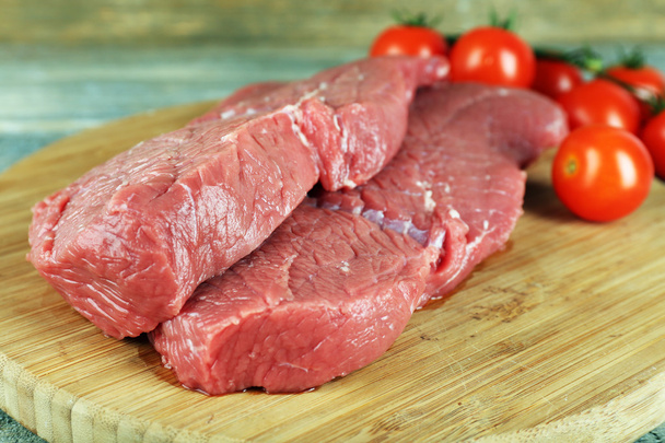 Raw beef steak with cherry tomatoes on cutting board on wooden background - 写真・画像