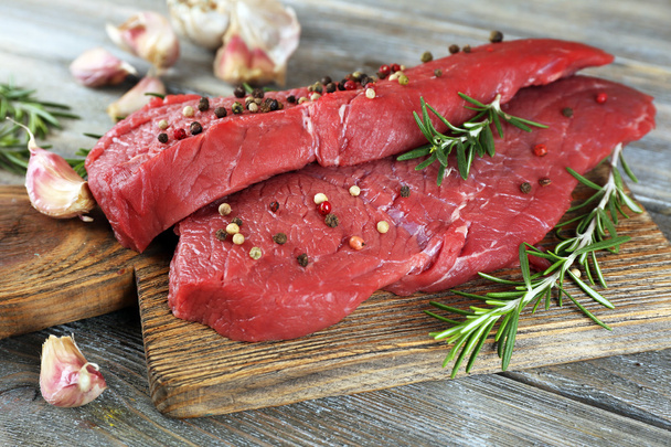 Raw beef steak with rosemary and garlic on cutting board on wooden background - Fotoğraf, Görsel