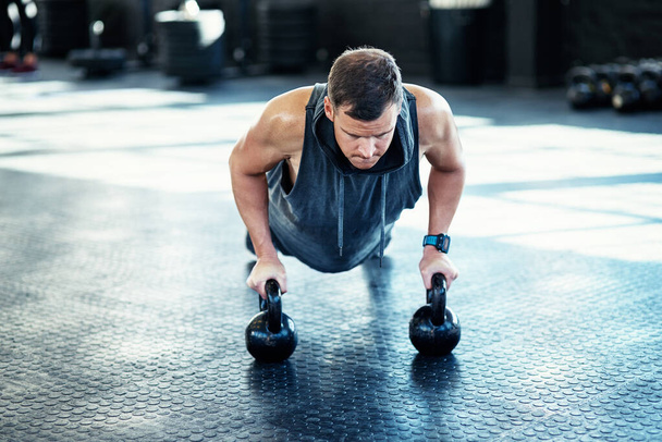 Trein om niet hetzelfde te blijven. een jonge man doet push-ups met kettlebells in een sportschool - Foto, afbeelding