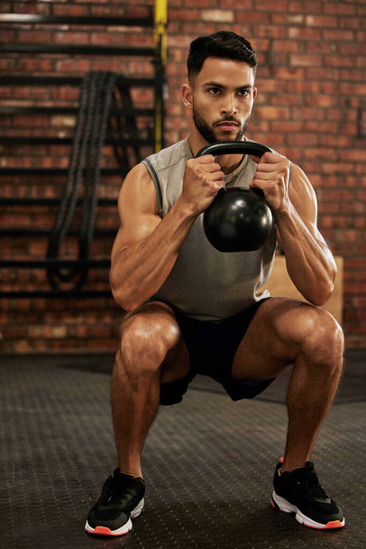 Bodybuilder, fitness and man with kettle bell in gym for exercise, strength training and workout. Sports, challenge and serious male person squat with weights for wellness, healthy body and muscles. - Foto, Imagen