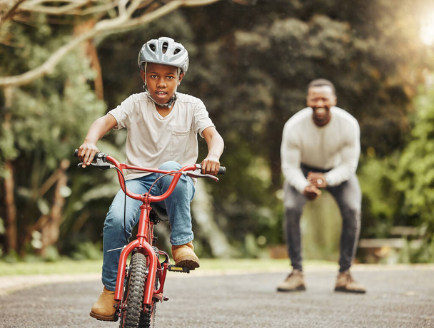 Bisikletli çocuk, baba tezahürat yapıyor ve bisikletçiliği öğreniyor. Güvenliği ve ailesi için parkta kask takıyor. Destek, motivasyon ve güven, siyah adam ve genç çocuk dışarıda bisiklet sürmeyi öğretiyor ve öğreniyor.. - Fotoğraf, Görsel