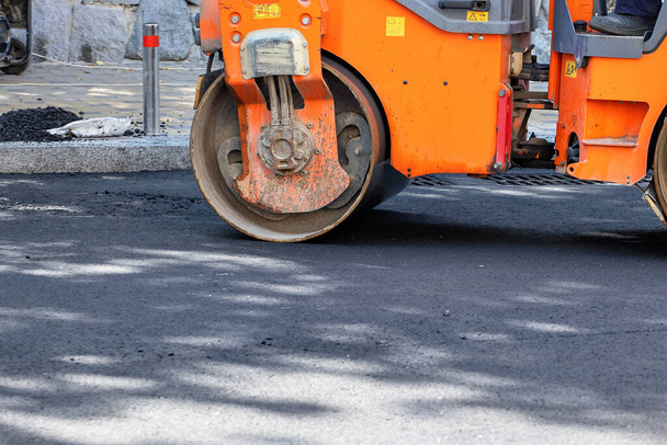 Zware trilwals op asfalt beton werken. Een fragment van een rolwiel, een stadsweg is in aanbouw, asfalt is in uitvoering. Kopieerruimte. - Foto, afbeelding
