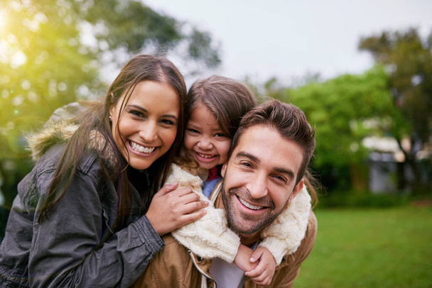 Family, piggy back and park portrait with a mom, dad and girl together with happiness and smile. Outdoor, face and summer vacation of a mother, father and kid with bonding, parent love and child care. - 写真・画像