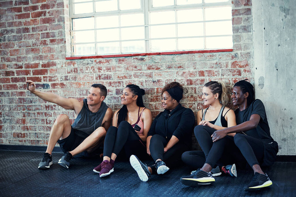 One last photo. a cheerful young group of people sitting down on the floor and taking a self portrait together in a gym - Foto, Bild