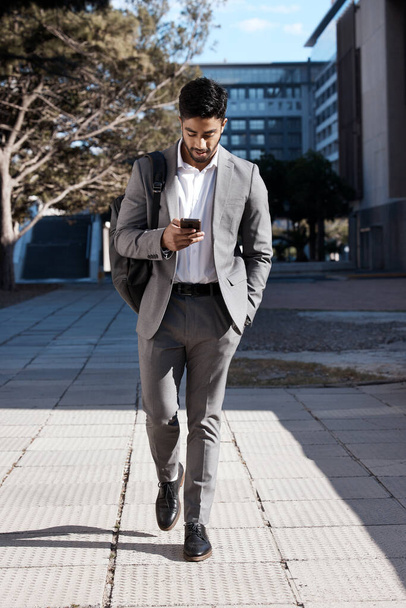 Phone, city and Indian business man walking for travel, social media or internet search. Smartphone, texting and male person on walk in town while checking app, message or text on commute in street. - Foto, afbeelding