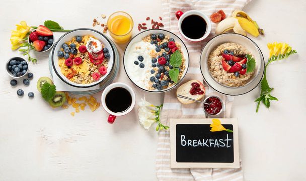 Breakfast food table. Healthy breakfast or brunch set, meal variety with granola, porridge, cornflakes, fresh berries, fruits and various of topping on a white background. Top view. - Photo, Image