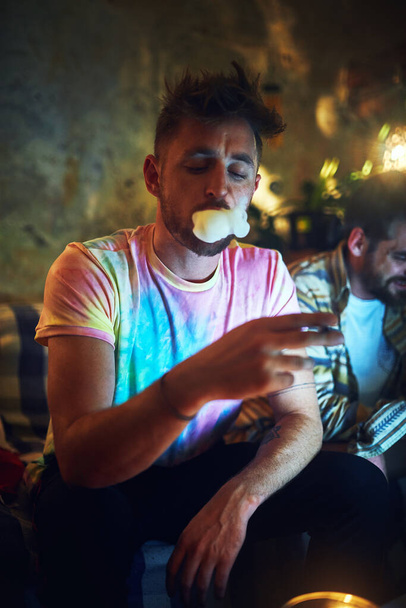 A ser tocado num sábado à noite. um jovem bonito fumando cannabis enquanto se senta com seu amigo em casa - Foto, Imagem