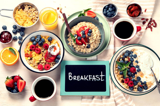 Breakfast food table. Healthy breakfast or brunch set, meal variety with granola, porridge, cornflakes, fresh berries, fruits and various of topping on a white background. Top view. - Foto, Imagem