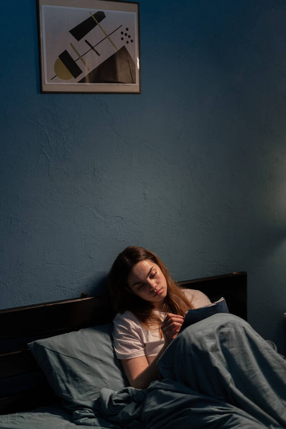 Smutna przygnębiona kobieta siedząca w łóżku i pisząca notatki w swoim dzienniku. Nieszczęśliwa dziewczyna, ma złe doświadczenie, czuje się w złym nastroju. Przestrzeń kopiowania - Zdjęcie, obraz