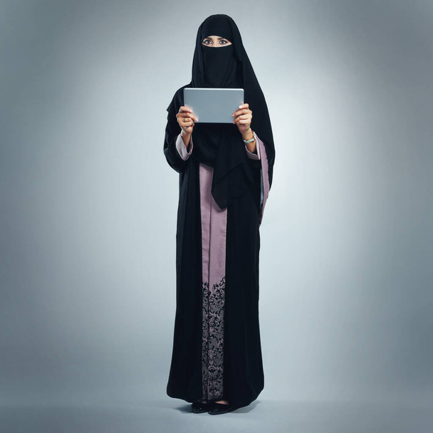 Si c'est nouveau, je le saurai. Portrait studio d'une jeune femme portant une burqa et utilisant une tablette numérique sur fond gris - Photo, image
