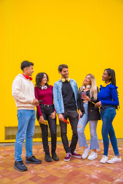 Portrait of a group of smiling young multi-ethnic teenage friends using cell phones on a yellow background. Technology addicted millennial community concept - Photo, image