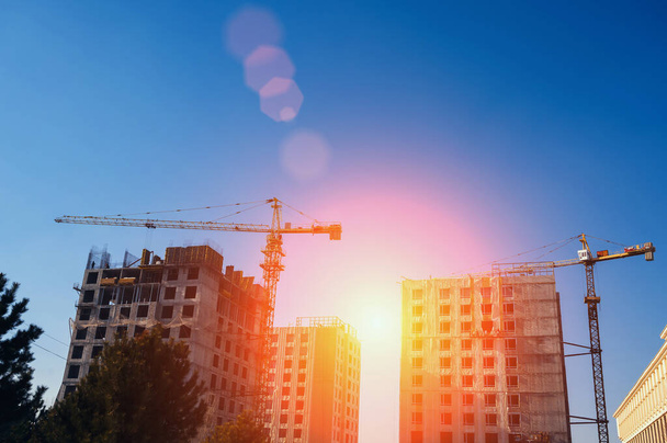 grúa de construcción está construyendo un edificio residencial en un sitio de construcción sobre el fondo del cielo azul con el sol - Foto, imagen