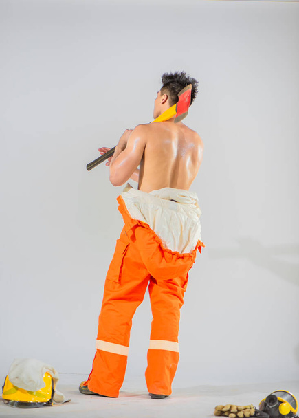 Профессиональный пожарный уверенно поворачивается спиной, демонстрируя свою силу и готовность, с железным топором на плече.. - Фото, изображение