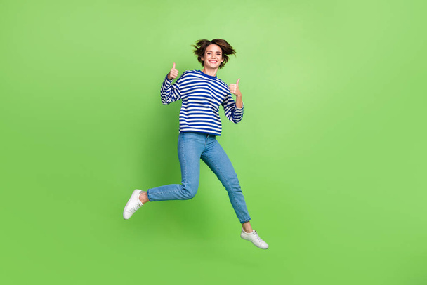 Full length photo of youngster woman jumping shopaholic thumbs up recommend new active vacation advert isolated on green color background. - Φωτογραφία, εικόνα