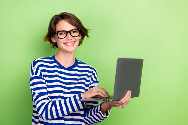 Photo of toothy beaming intelligent girl short haircut dressed sailor long sleeve holding laptop isolated on green color background. - 写真・画像