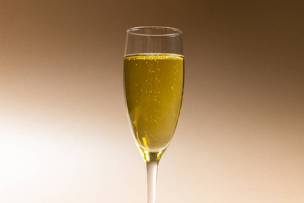 Close-up of champagne in champagne flute isolated against brown background, copy space. Yellow, drinking glass, bottle, alcohol, drink, liquor and celebration concept. - Foto, Bild